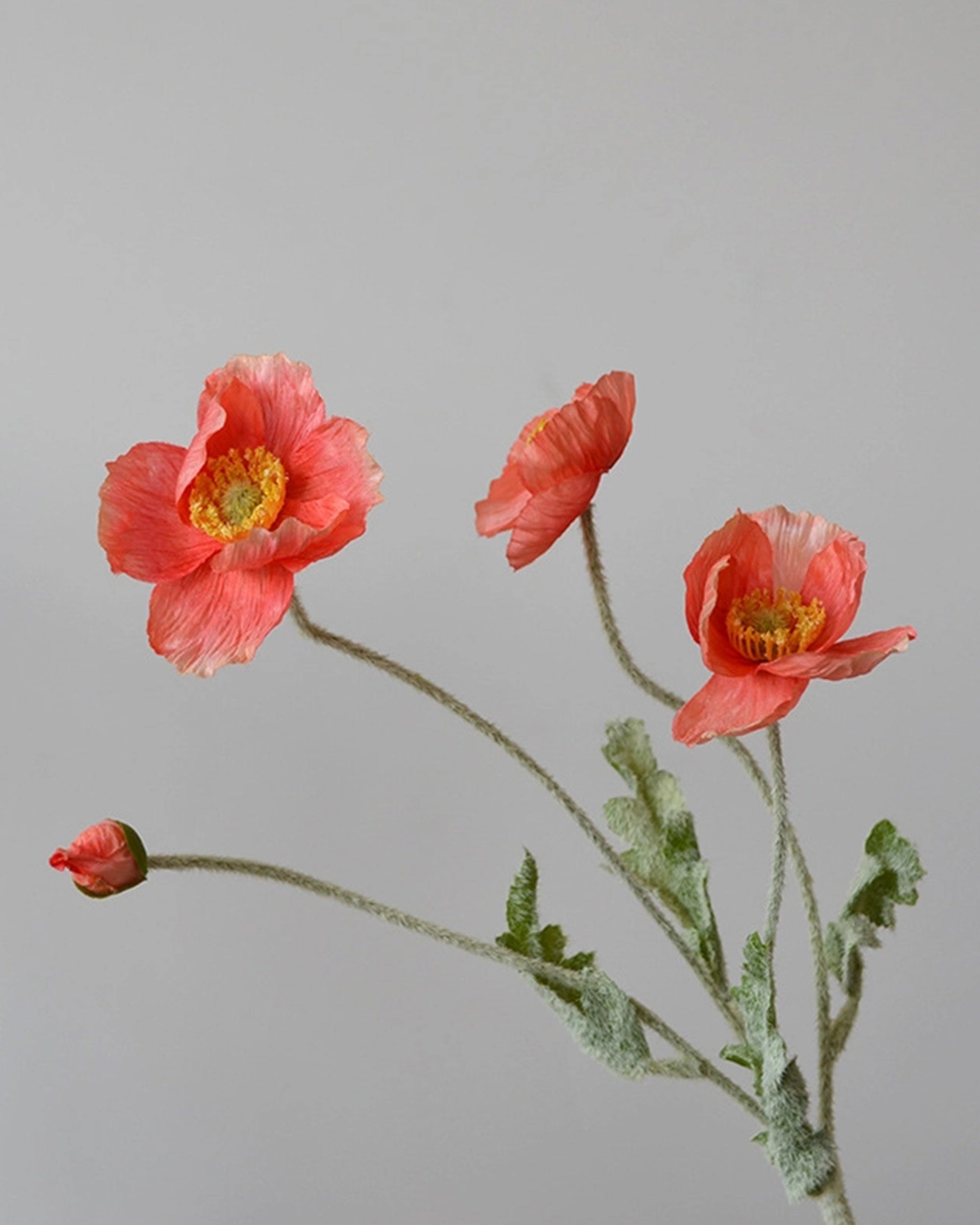The Faire 22'' Single Flocked Floral Poppy Spray features vibrant orange blooms and one bud on green, textured stems—perfect artificial flowers to brighten any space against a light grey background.