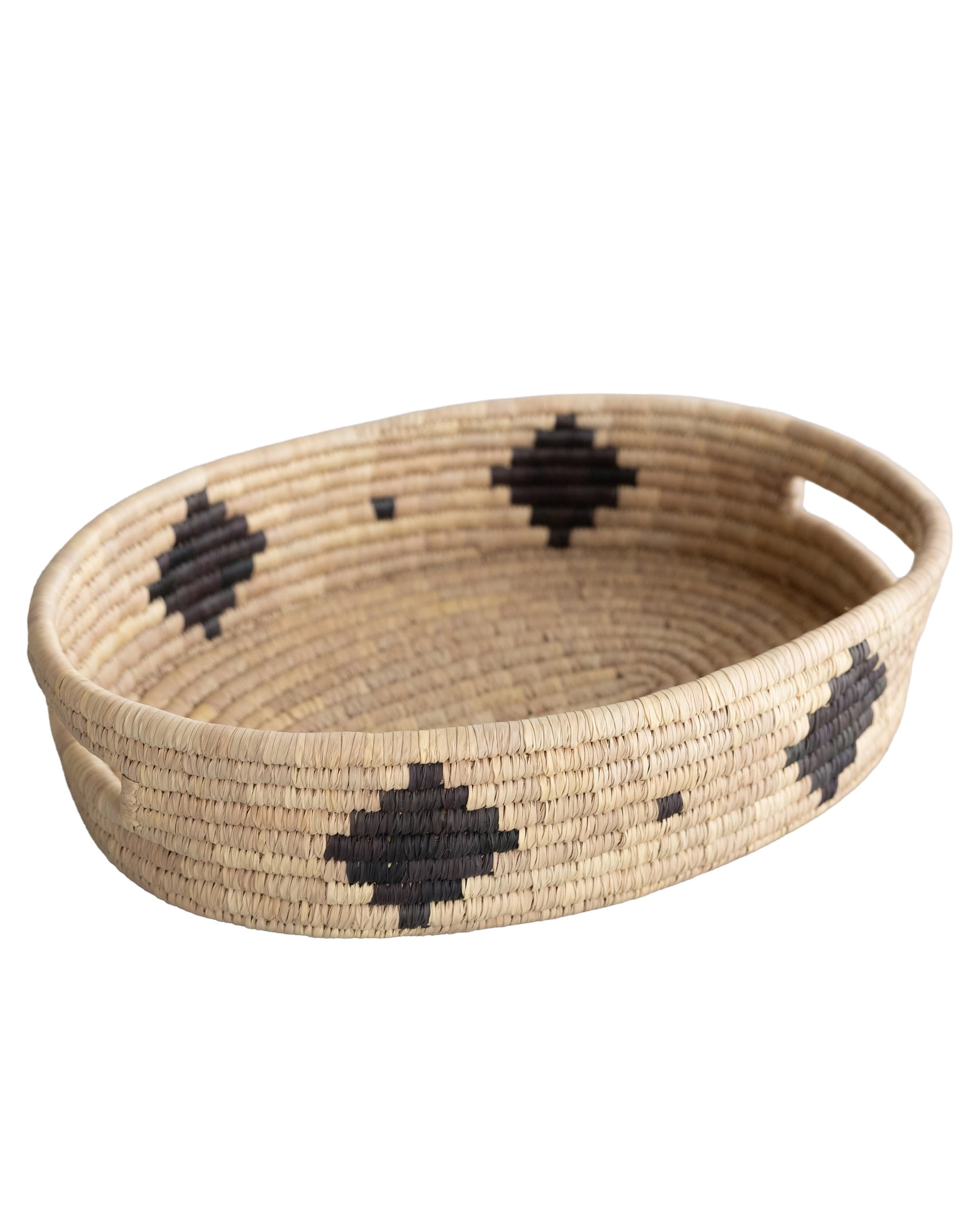 The Faire Palm Leaf Oval Basket is a shallow, handwoven tray with two handles, featuring a natural tan color and bold black geometric patterns—expertly crafted by fair trade artisans.