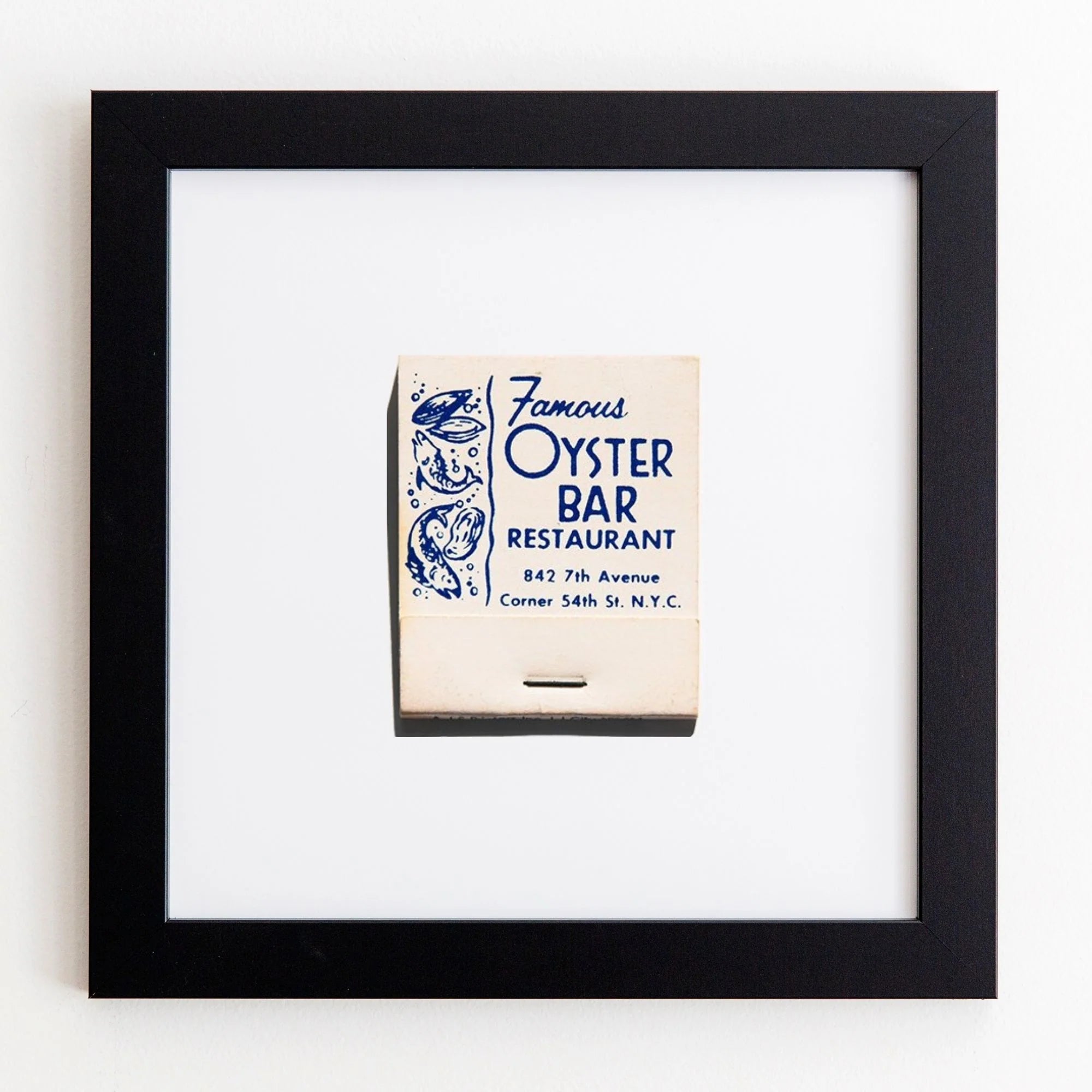 A framed matchbook cover from Match South&#39;s &quot;Famous Oyster Bar Restaurant&quot; displaying its address and decorative marine life illustrations on a white Bungalow-style wall in an Art Square Black Frame.