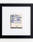 A framed matchbook cover from Match South's "Famous Oyster Bar Restaurant" displaying its address and decorative marine life illustrations on a white Bungalow-style wall in an Art Square Black Frame.