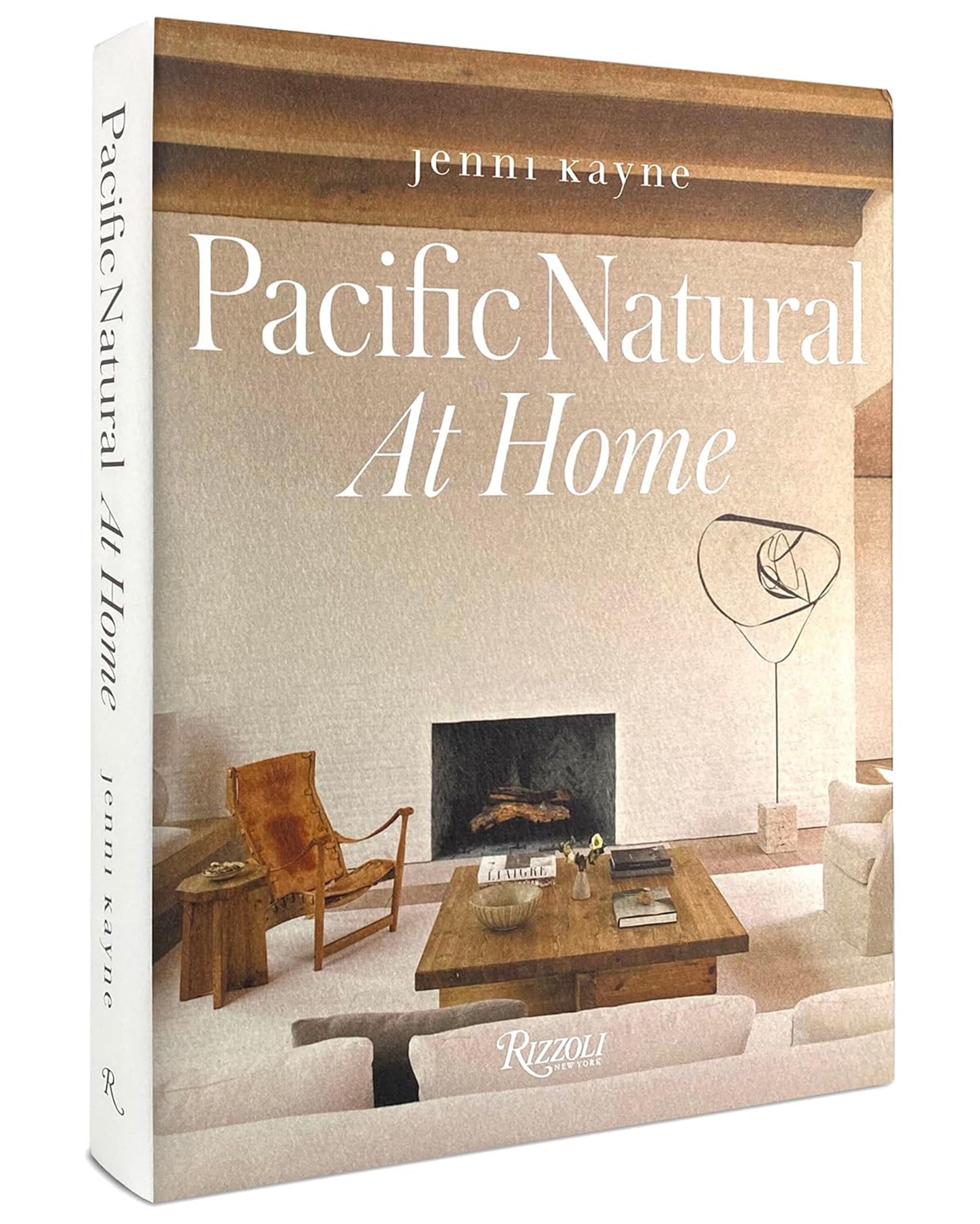 Pacific Natural At Home" by Random House highlights natural design in a minimalist home, featuring neutral furniture, a fireplace, wooden coffee table, and modern art.