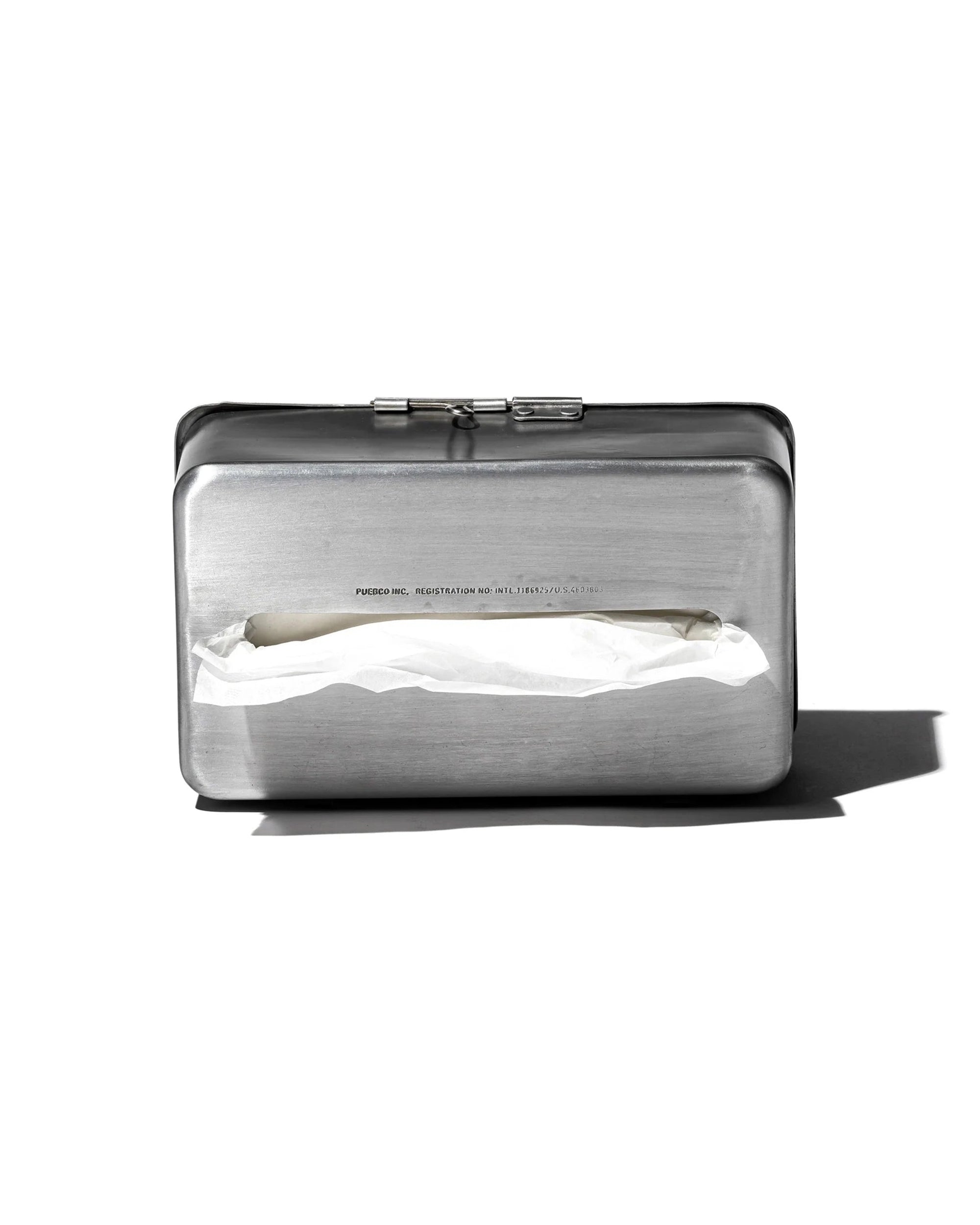 The Faire Paper Towel Wall Case is a silver aluminum tissue dispenser with a matte finish and rectangular design, featuring a slot that reveals a partially pulled tissue, casting a shadow on a white background.