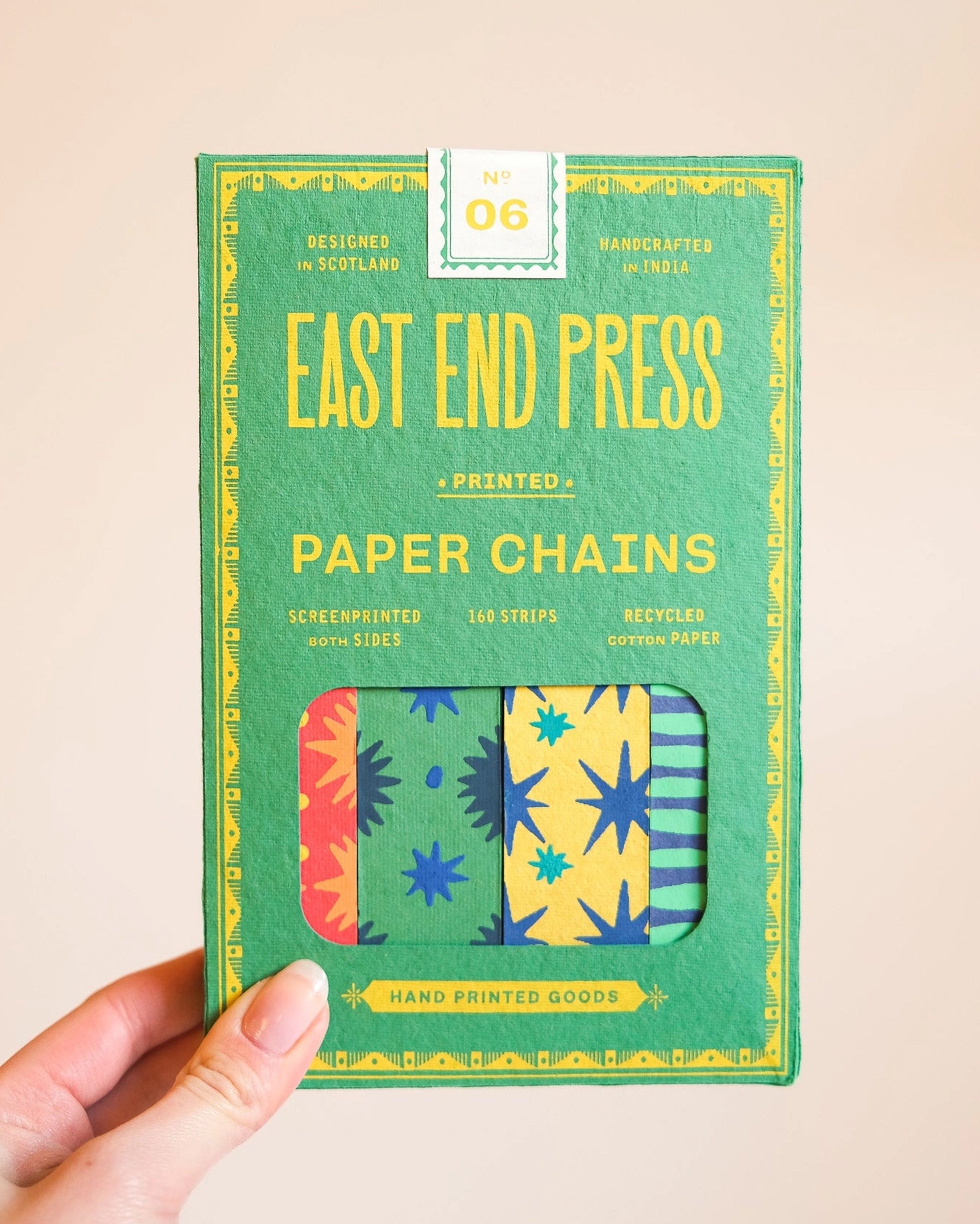 A hand holds a box labeled "Faire Paper Garland/Chains," featuring colorful star and geometric designs—ideal for vibrant decorations or festive birthday garlands. The green packaging displays yellow, blue, and orange text.