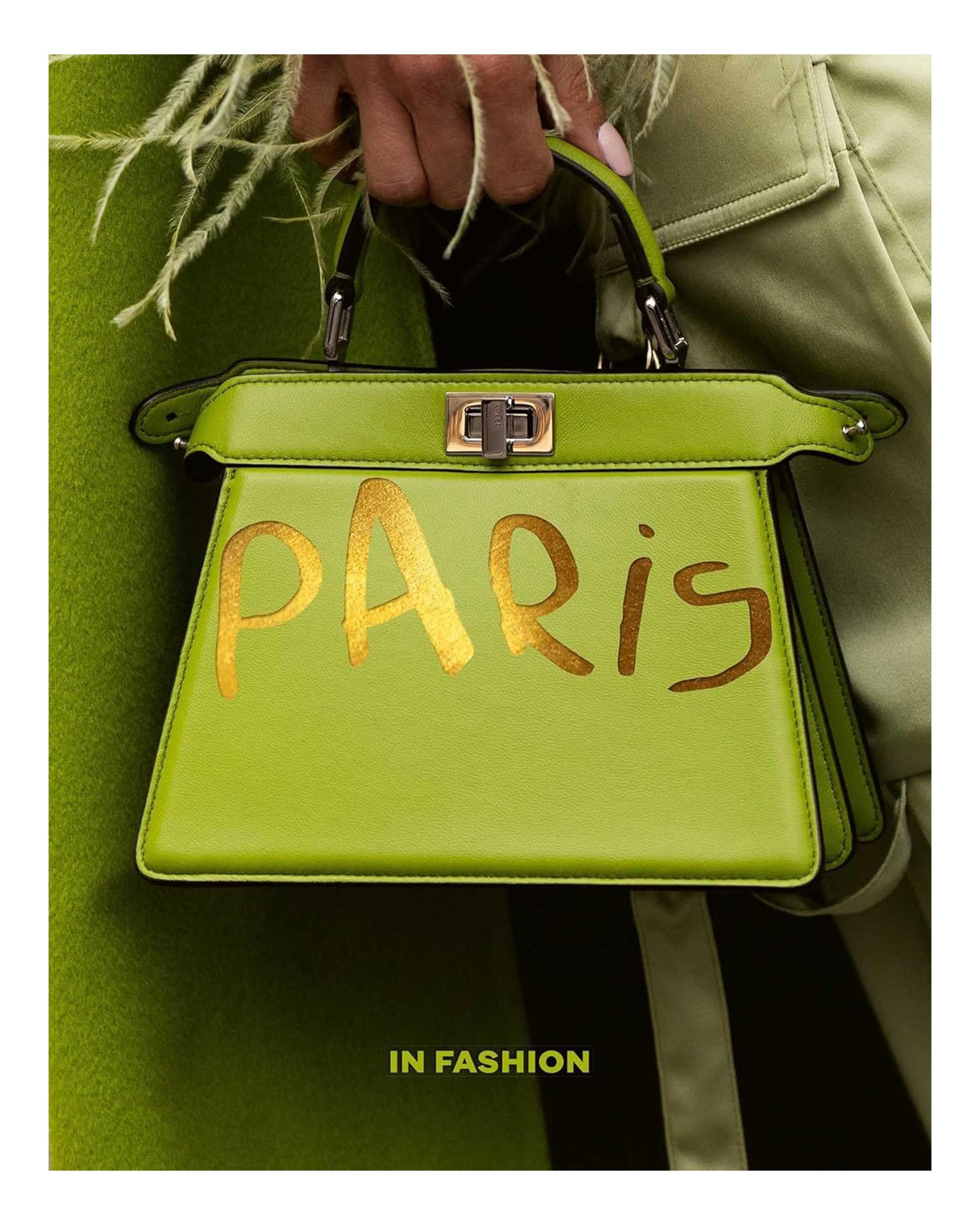 A person in green holds the "Paris In Fashion" handbag by Simon & Schuster Inc., featuring "PARIS" painted in gold, celebrating Parisian style. The phrase "IN FASHION" is displayed at the bottom of the image.