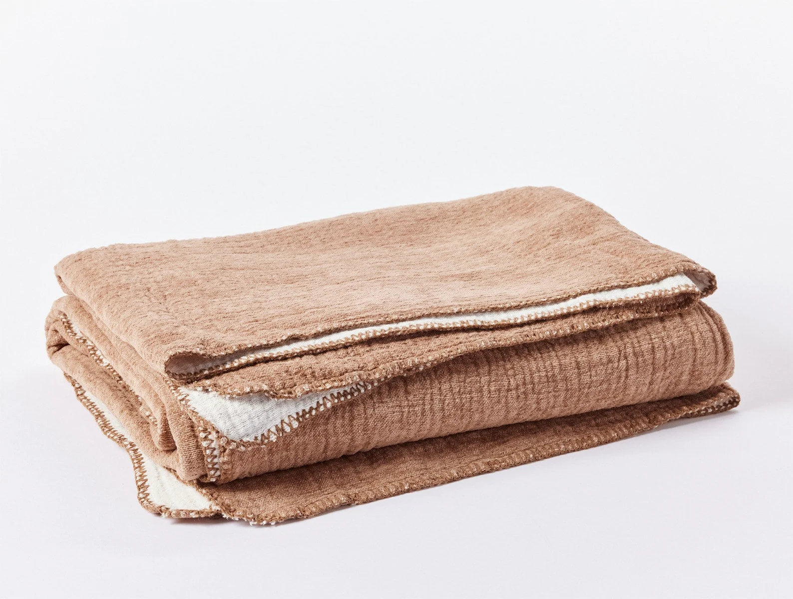 The Cozy Cotton Org. Blanket by Coyuchi Inc is a folded, soft brown organic cotton chenille blanket with white edging on a white surface, providing lightweight warmth.