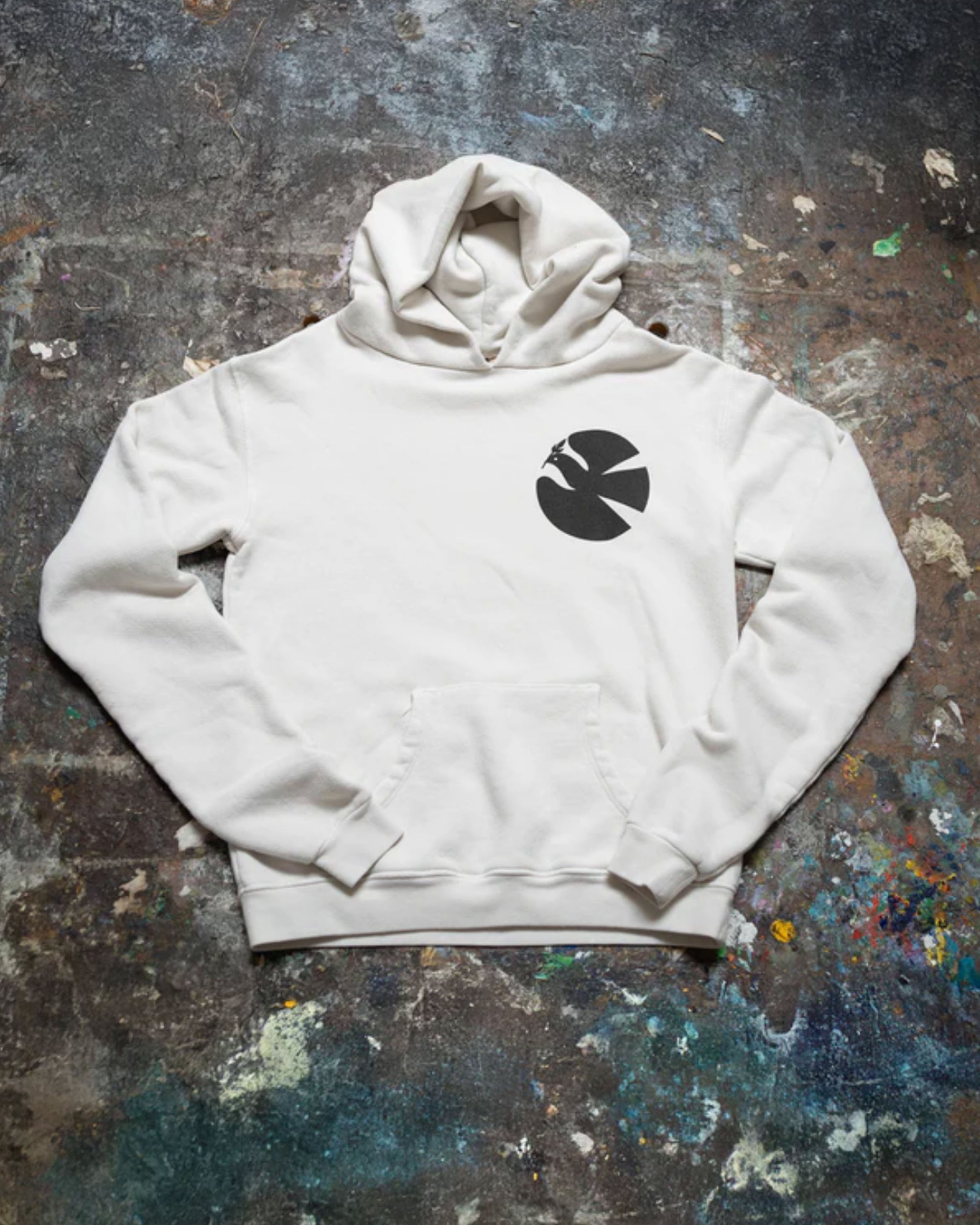 The Made Worn Peace Love Oversized Hoodie, featuring a black circular logo on the left chest, is displayed flat on a colorful, paint-splattered concrete surface—perfect as a winter sweatshirt for Peace Love Art enthusiasts.