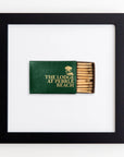 A framed acrylic display featuring a dark green book titled "The Lodge at Pebble Beach" with its spine exposed, revealing a series of matches integrated into the book design, against a white background by Match South's Art Square Black Frame.