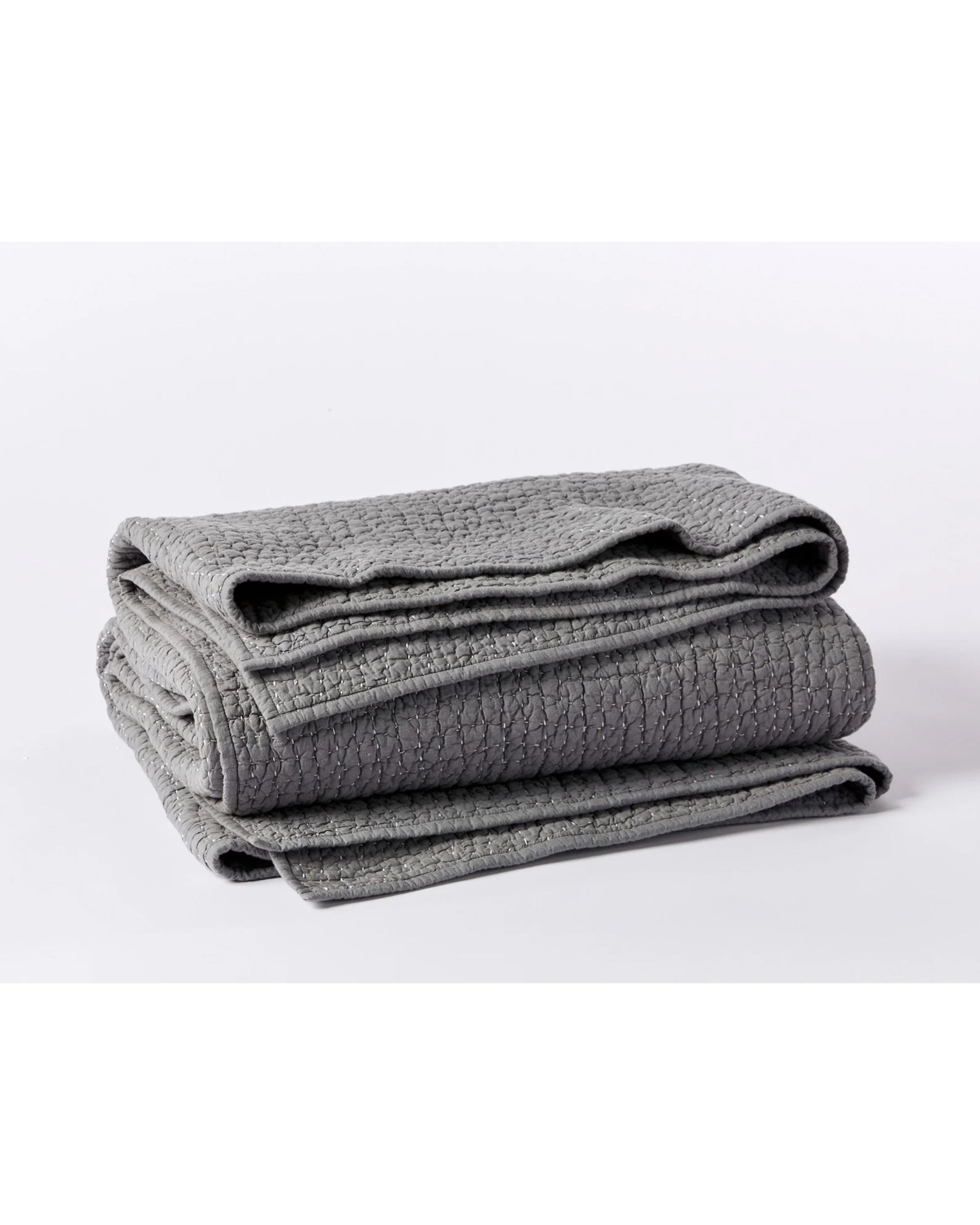 A Coyuchi Inc Pebbled Org Quilt Queen in Slate is folded and stacked on a white surface.