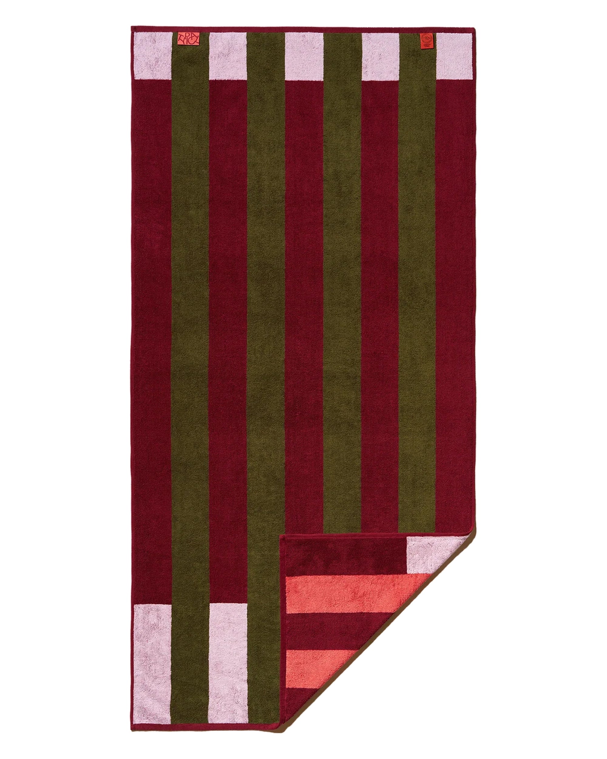 The Typical Pink/Burgundy Stripe Bath Towel is rectangular, reversible, and features bold vertical stripes in burgundy and olive green, plus a small pink and red striped section at one corner.