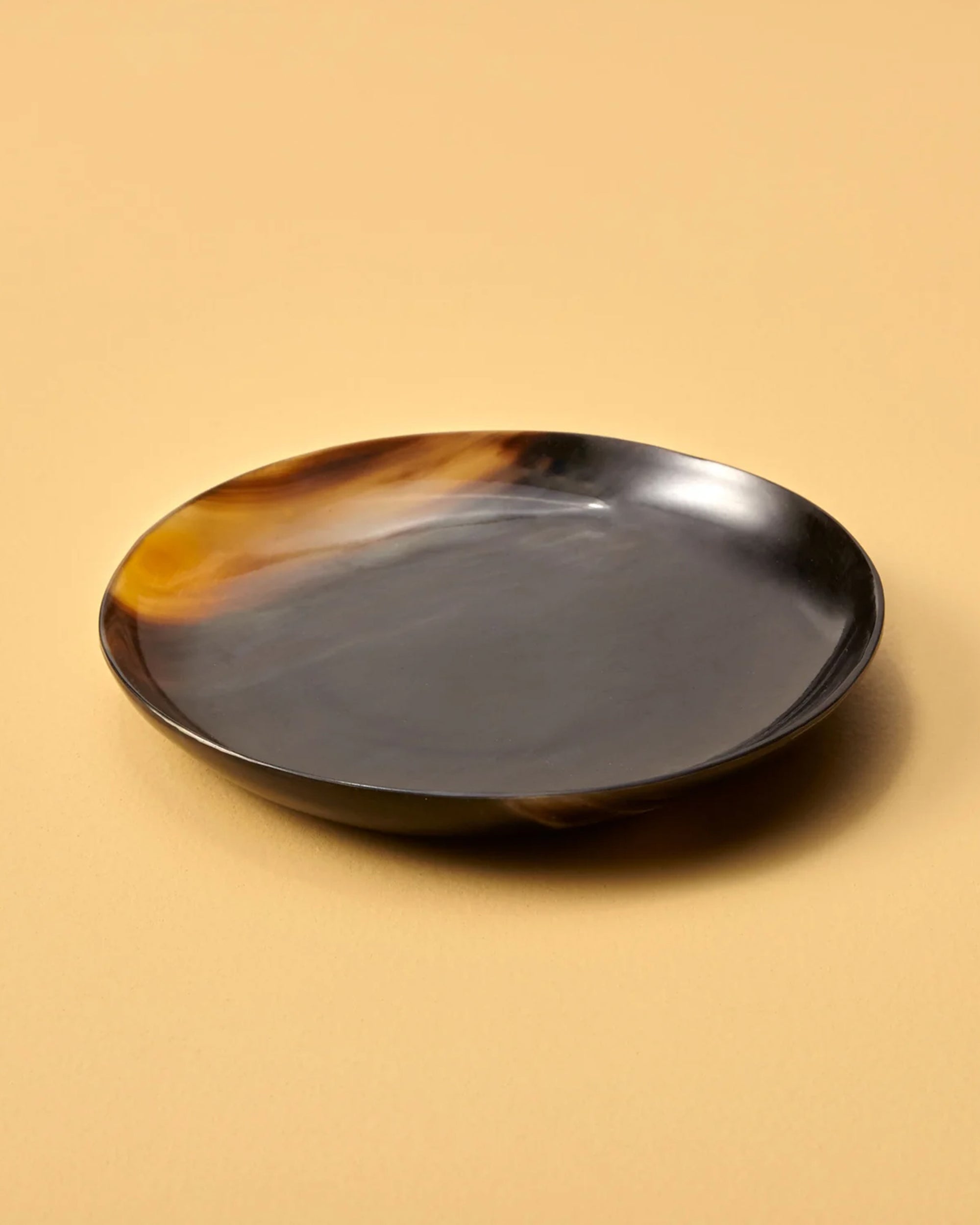 The Be Home Horn Plate S is a handcrafted, round, shallow plate with a glossy dark brown and amber swirl—an ethical accent for your home decor.