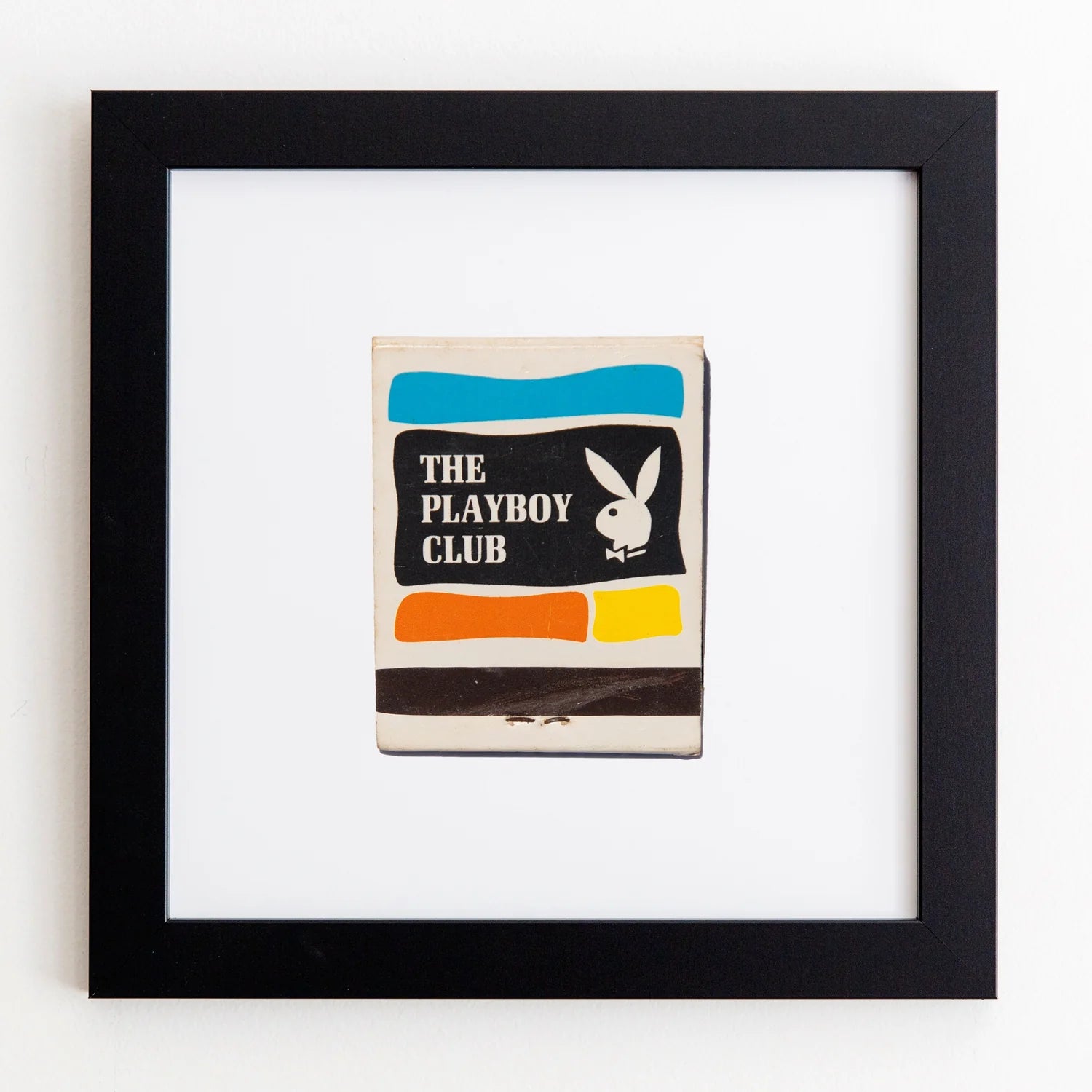 A framed vintage Match South matchbook cover, featuring the iconic Playboy bunny logo and horizontal stripes in blue, black, and orange, mounted on a white background within an Art Square Black Frame.