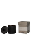 A black ADLAN Candle with a lid and two wicks sits beside a beige "ADLAN" box. The minimalist design by ADLAN Fragrances evokes luxury, blending soft violet and ripe plum notes for an elegant home scent.