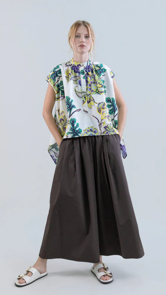 A woman wears the Psophia Air Drift Wide-Leg Culotte with Drawstring Waist, a loose, dark brown cotton poplin culotte, paired with a colorful floral sleeveless top and white slide sandals, standing against a plain light background.