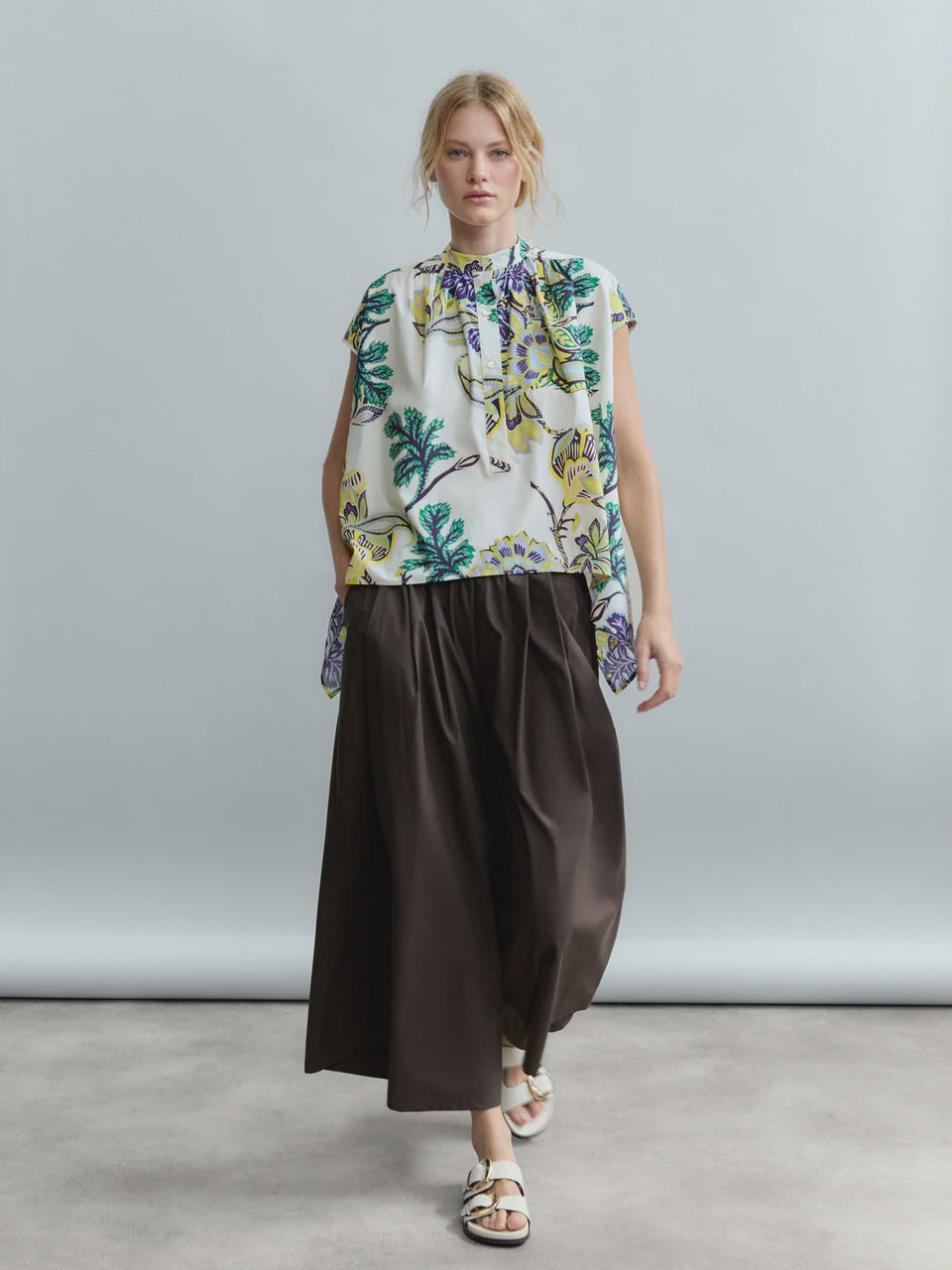 A person wears Psophia's 2684 Womens Trouser with a sleeveless, floral cotton poplin blouse featuring a ruffle neckline and white sandals, standing against a light gray background.