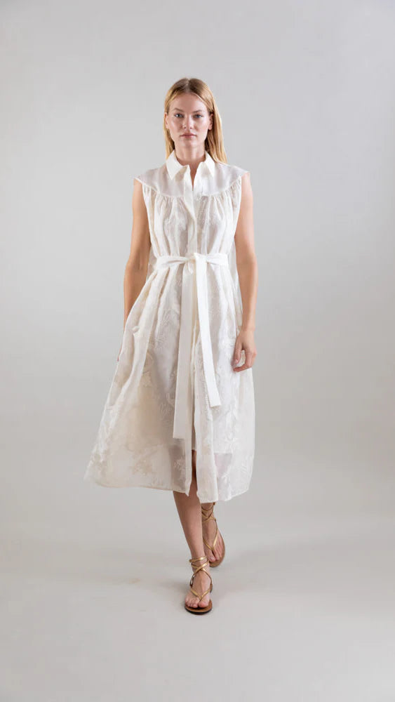 A woman stands against a plain background wearing the Psophia Ethereal Botanical Tencel Shirt-Inspired Dress, featuring an A-line silhouette, embroidery, a tied fabric belt at the waist, and sandals. She looks directly at the camera with a neutral expression.