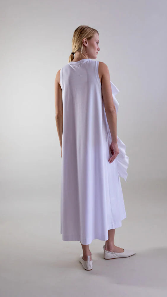 A woman with blonde hair in a low ponytail wears the Psophia Sculptural Rosette Mercerized Cotton Midi Dress in white and matching flat shoes, standing on a light background and facing slightly away from the camera.