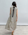 A woman with long dark hair stands on a gray floor, facing away, wearing the Psophia Soft-Touch Plaid A-Line Drop-Waist Dress against a light gray background.