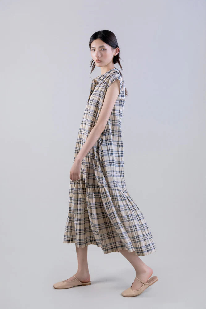 A woman stands sideways in a Psophia Soft-Touch Plaid A-Line Drop-Waist Dress, sleeveless and ankle-length, styled with beige slip-on shoes against a plain light gray background.