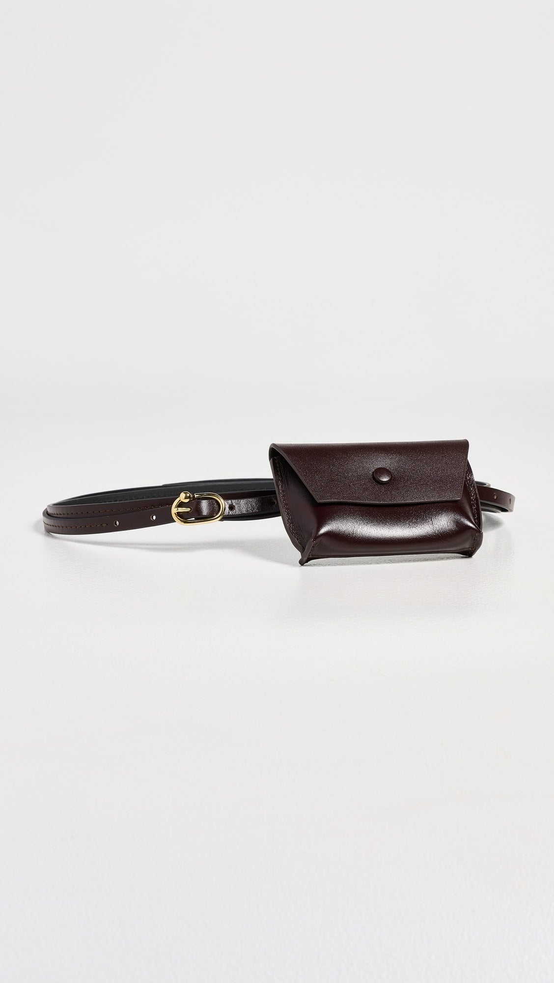 The Rachel Comey Double Wrap Hamcon Belt w/ Pouch is a small, dark brown calfskin belt bag with a flap and gold-tone hardware, shown laid flat on a white surface.