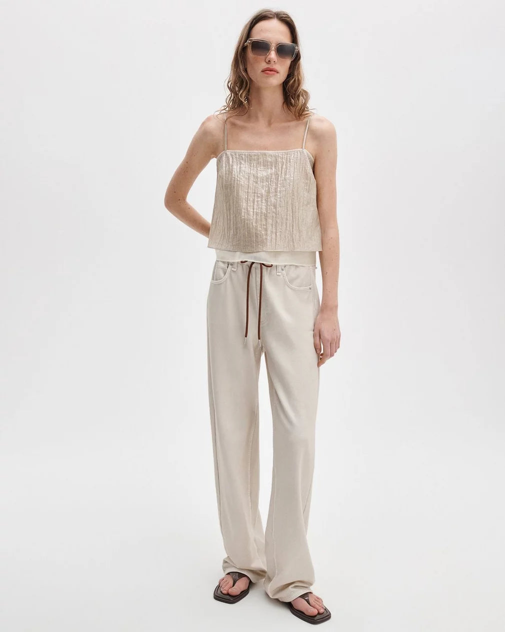 A woman in Rag &amp; Bone rb miramar trry drwcrd wde leg pants, sunglasses, a beige spaghetti-strap top, and black flip-flops stands against a plain white background.