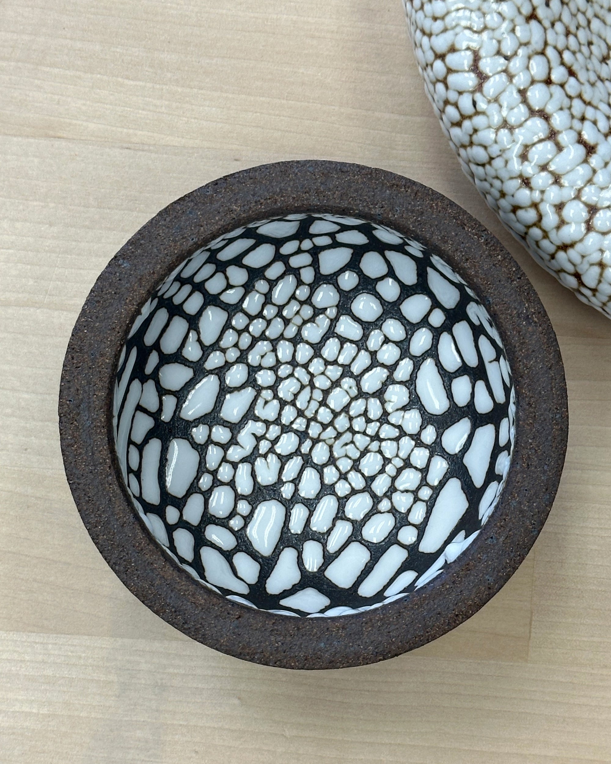 The Ritual Bowls 4.5" by Faire feature a round ceramic design with a dark brown rim and white interior accented by an irregular black-outlined crackle pattern—perfect as versatile bowls or chic salt cellars on light wood surfaces.