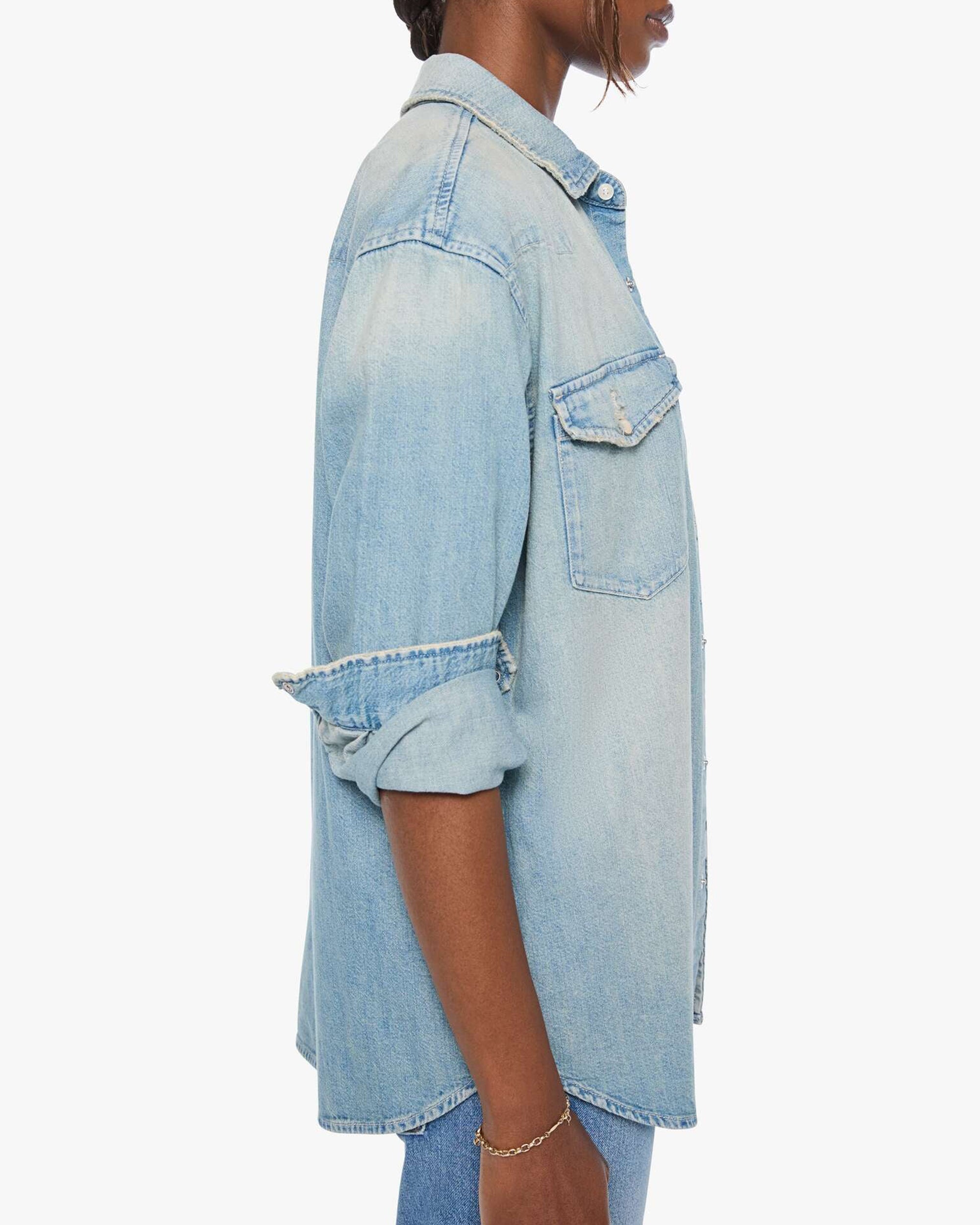 Oversized light blue denim shirt by Mother, sleeves rolled up, shown in side profile view.