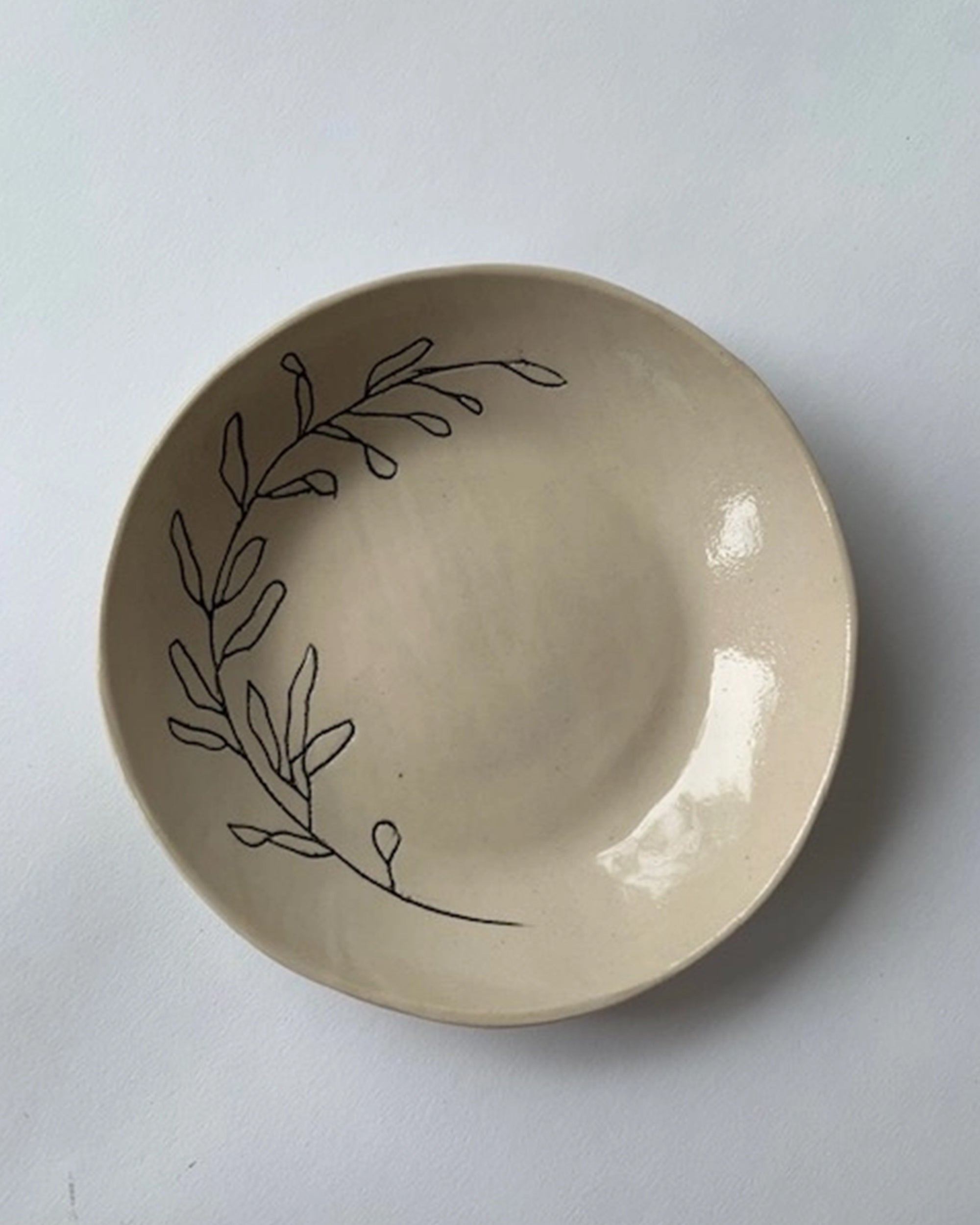 The Faire Ring Bowl is a cream-colored ceramic catch-all featuring a simple black line drawing of leafy branches, showcasing botanical symbolism in its design.