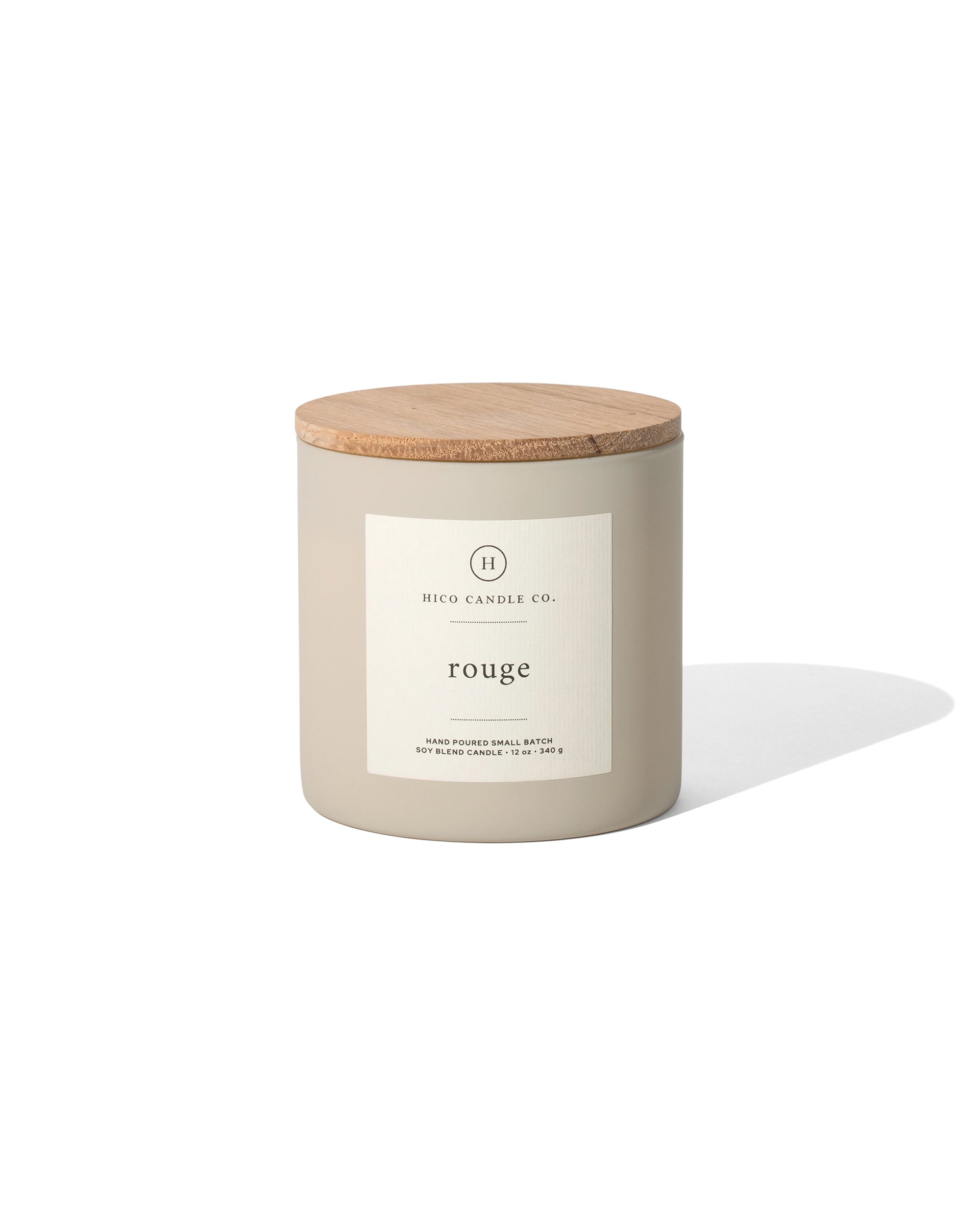 A beige 14oz. Rouge candle by Faire, featuring a wooden lid and white label, crafted from soy wax and inspired by Baccarat Rouge 540, is set against a white background with a soft shadow on the right side.