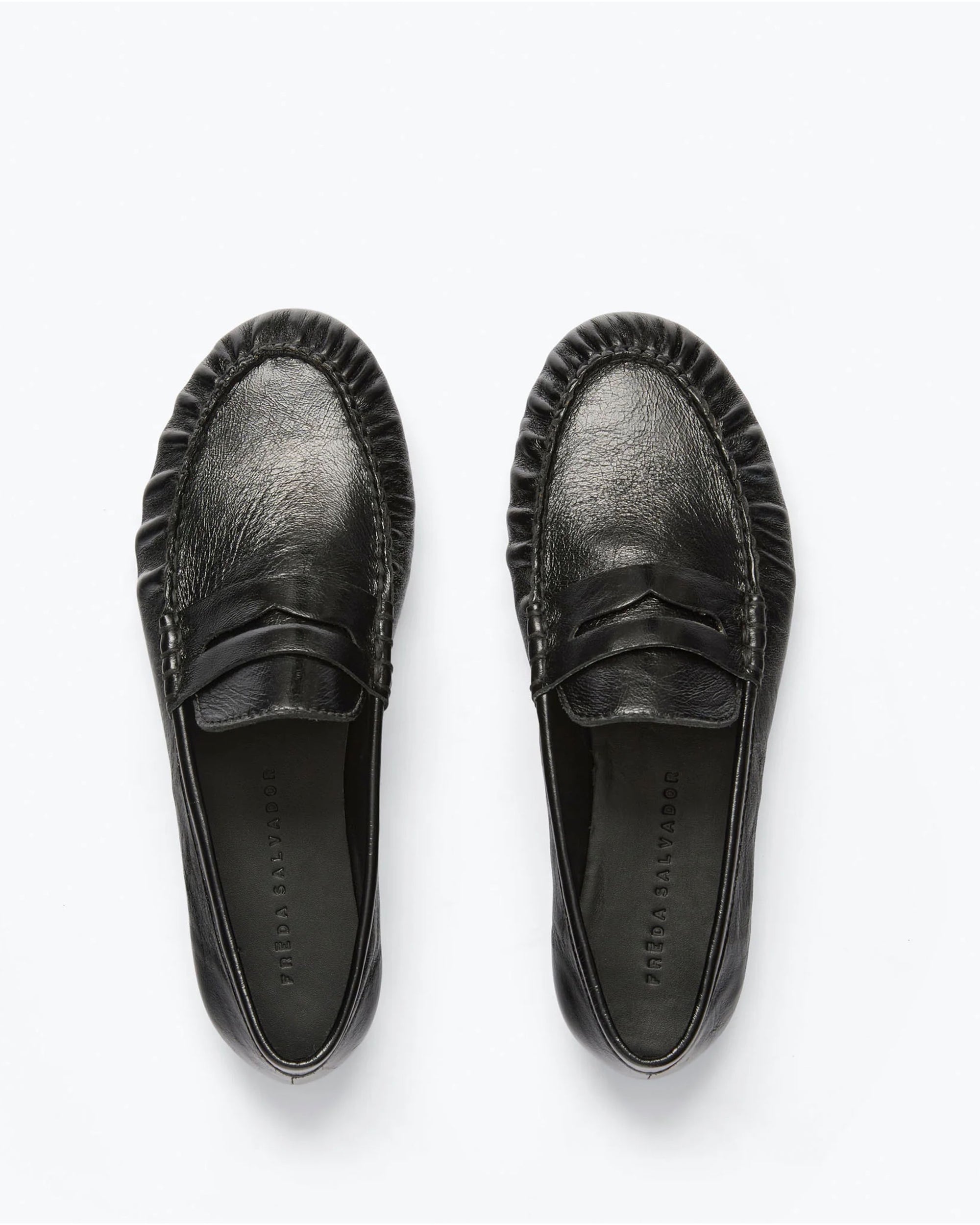 The Freda Salvador Sydney Crinkle Loafer features black Italian leather, gathered toe stitching, and a simple front strap, shown on a white background.