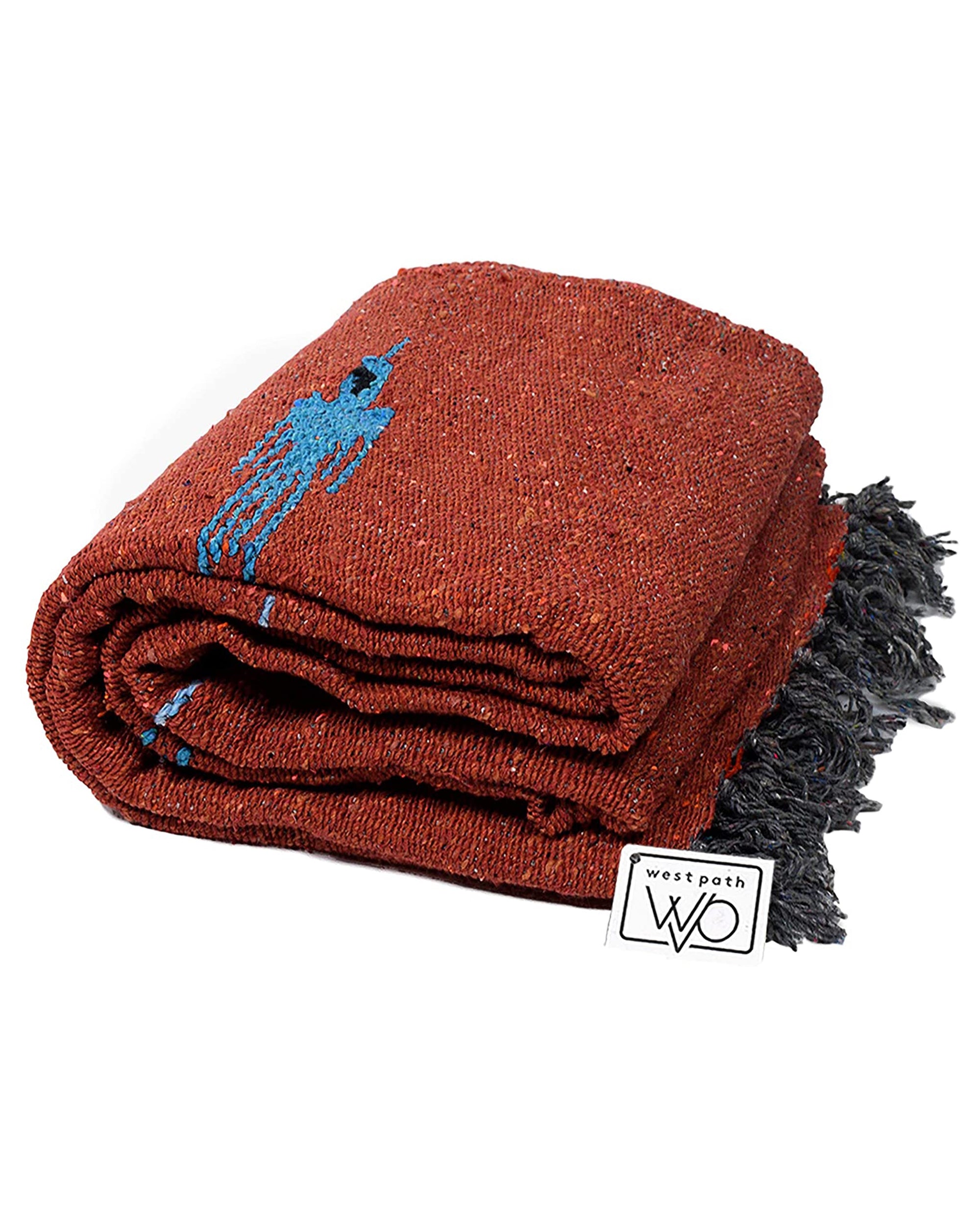 The Faire Rust Red Baja Thunderbird Mexican Blanket features a rust hue with black fringe, a small blue design, and a white "west path WO" tag. Handmade in Mexico.