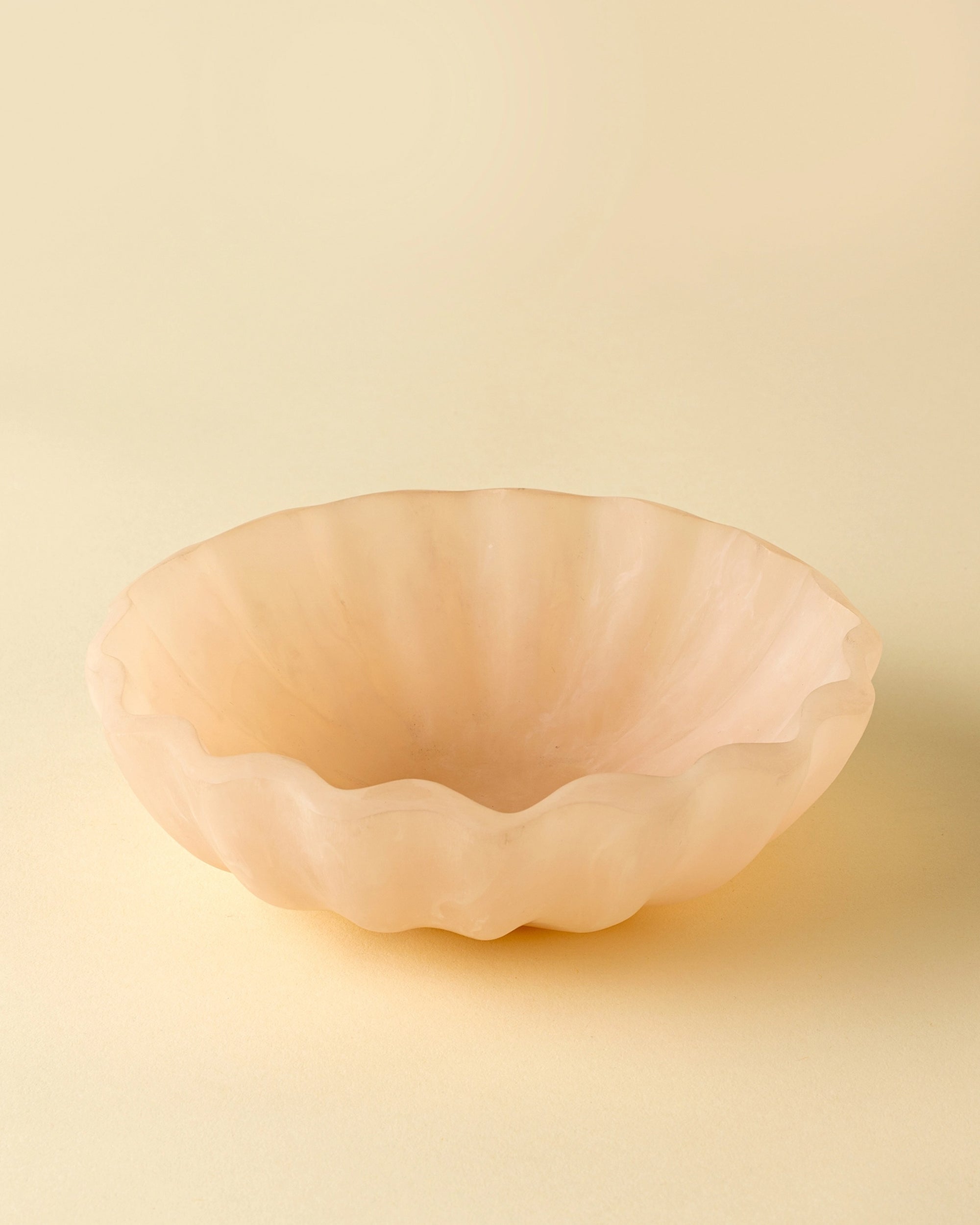 The Indaba Scallop Resin Bowl, in light peach with wavy scalloped edges, features a smooth matte surface and subtle opalescent finish, making it an elegant decorative piece for any space.