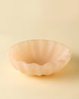 The Indaba Scallop Resin Bowl, in light peach with wavy scalloped edges, features a smooth matte surface and subtle opalescent finish, making it an elegant decorative piece for any space.