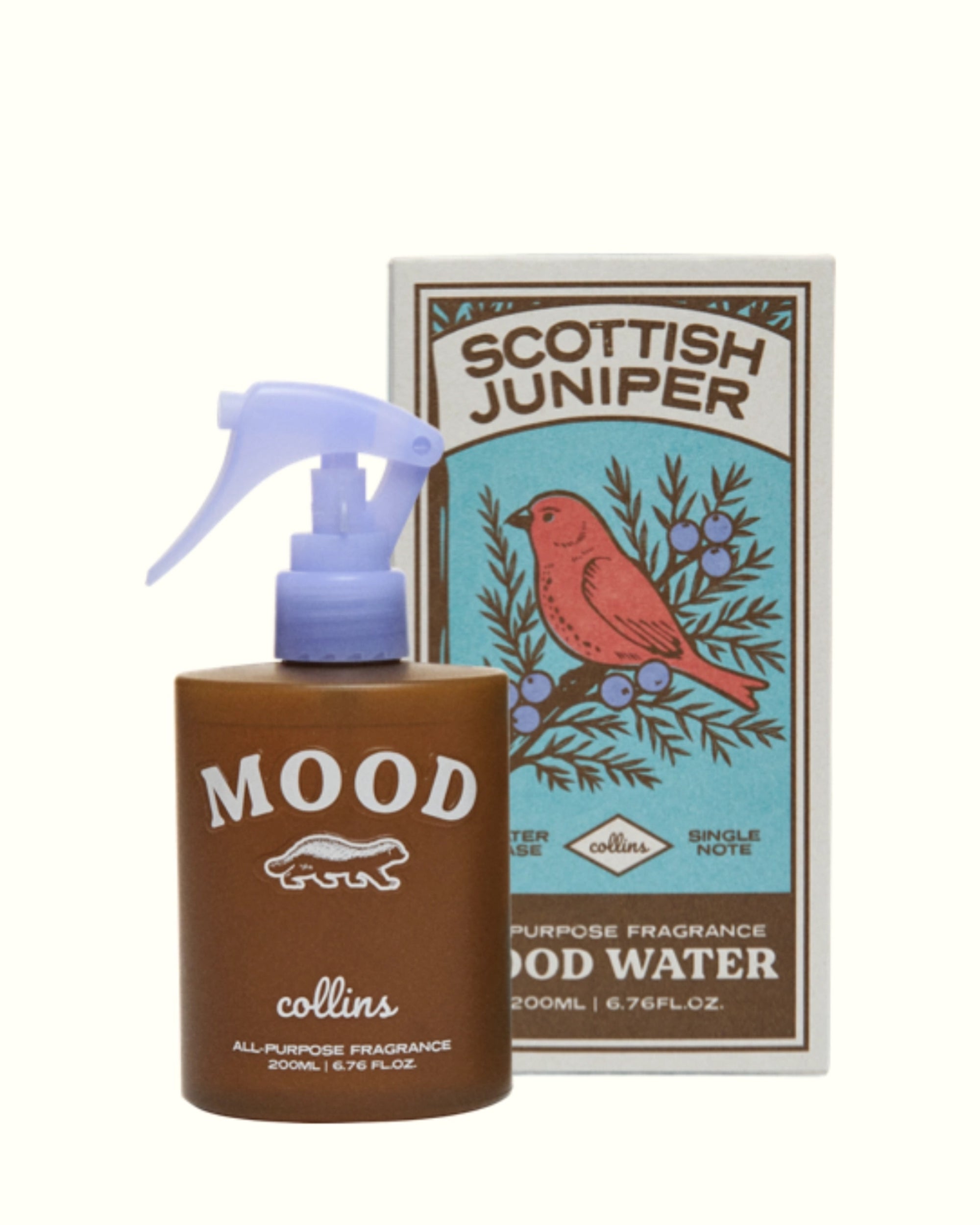 A brown spray bottle labeled "MOOD" by Faire stands before a box with a red bird and juniper berries, displaying "Scottish Juniper Room Spray"—a fabric safe, ethanol-free fragrance for any room.