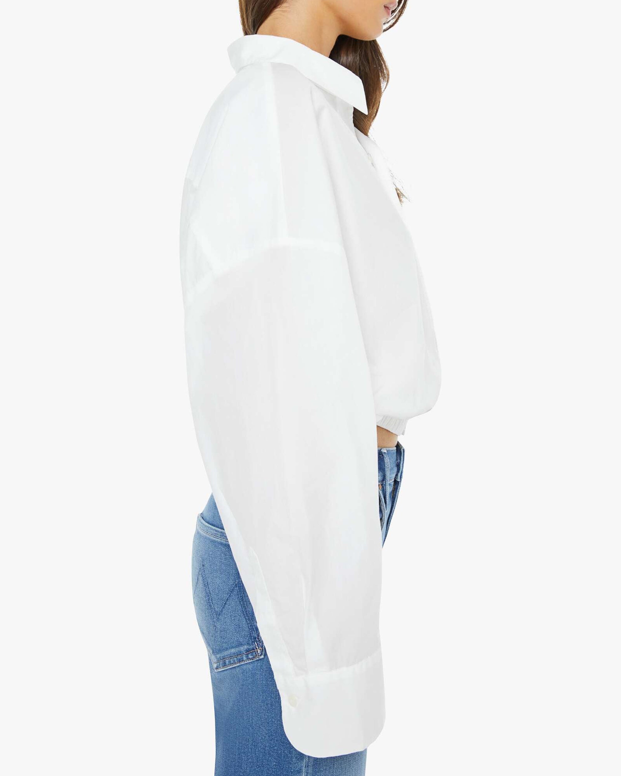 A woman in The Scrunchie Frenchie white cotton top by Mother and blue jeans stands in profile against a plain white background.