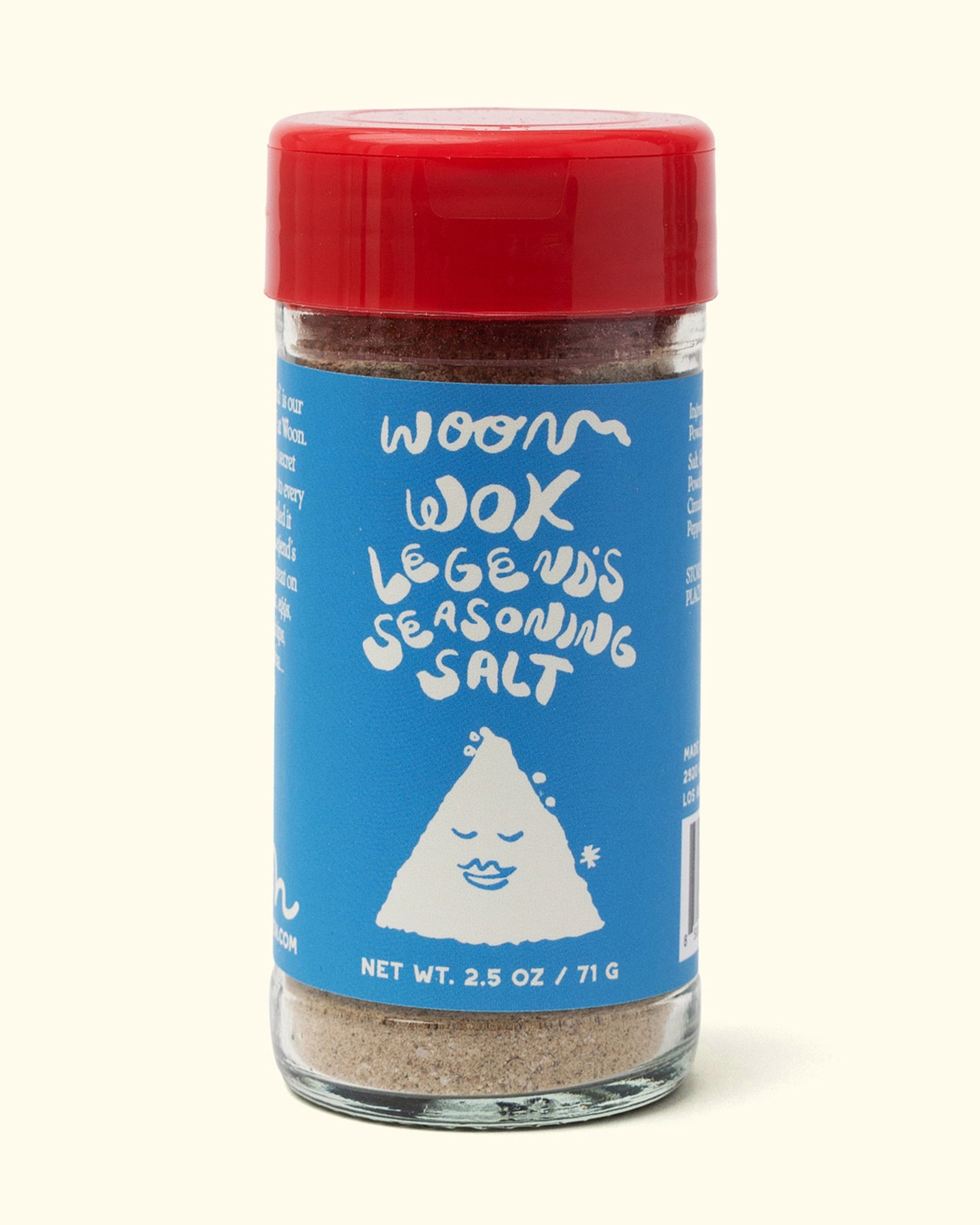 A glass jar of Faire's Woon Wok Legend's Seasoning Salt with a red lid and blue label featuring a smiling rice character. This 2.5 oz (71 g) blend adds bold flavor to any dish.