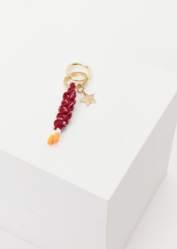 The Upside's LIMITLESS KEYRING features a gold keychain with a star charm, a red braided polyester cord, and two small orange beads, all displayed on a white block.