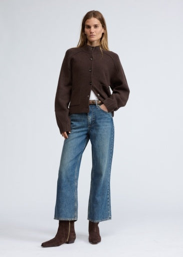 A woman stands against a plain background wearing the Rag &amp; Bone bridget mock neck cardigan, blue wide-leg jeans, and brown ankle boots. Her long straight hair and neutral expression capture effortless cold weather style.