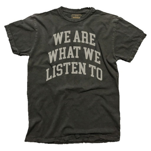 A vintage, unisex tee from Wildcat Retro Brands showcases a faded black design with the bold, arched text "WE ARE WHAT WE LISTEN TO" prominently displayed on the front. Made in the USA, this shirt seamlessly merges timeless style with cultural expression.