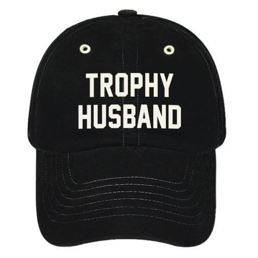 A vintage black baseball cap by Wildcat Retro Brands, featuring white embroidered text on the front that reads "TROPHY HUSBAND," and an adjustable buckle closure for a perfect fit.