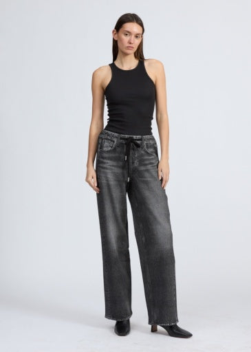 A woman with straight, long hair and a neutral expression stands against a plain background wearing Rag & Bone's miramar terry drwcrd wide pant—faded black wide-leg jeans with an elastic waist and drawstring—a fitted black sleeveless top, and black heeled shoes.