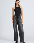 A woman with straight, long hair and a neutral expression stands against a plain background wearing Rag & Bone's miramar terry drwcrd wide pant—faded black wide-leg jeans with an elastic waist and drawstring—a fitted black sleeveless top, and black heeled shoes.