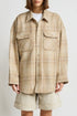 A person wears an oversized beige plaid Denimist RORY SHIRT JACKET with flap pockets over a white top and beige knee-length shorts, standing against a plain light background.