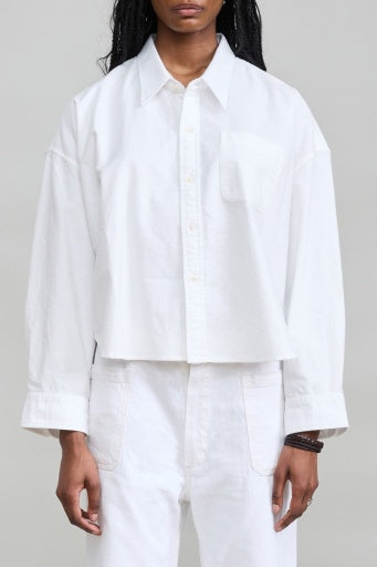Denimist cropped denim shirt with white pants, minimalist style against a plain gray backdrop.