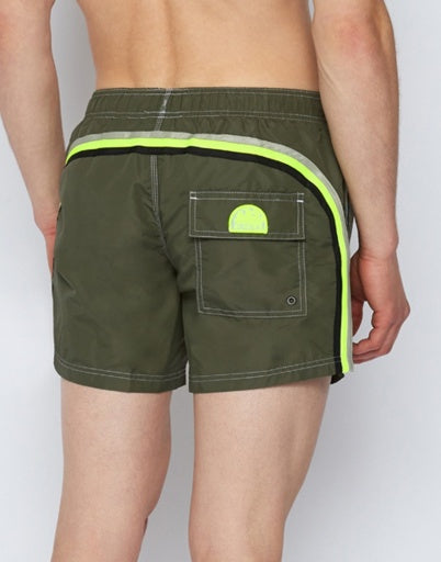 A person shown from behind wears SUNDEK/KickoffUSA 14" ELASTIC WAIST Board Shorts in olive green with a neon yellow stripe and a back flap pocket, posed against a plain background.