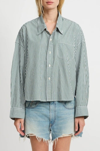 A person, head partially out of frame, wears Denimist's green and white striped CROPPED SHIRT with a front pocket, paired with frayed light-wash denim shorts.