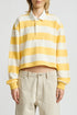 A person wearing the Denimist CHARLIE RUGBY, a yellow and white boxy fit cropped rugby top with a white collar, paired with loose beige pants, stands against a plain background.