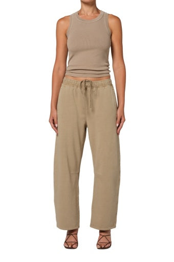 A person in Citizens Of Humanity/AGOLDE miro sweatpants, a fitted beige sleeveless cotton tank top, and brown strappy sandals stands against a white background.