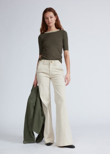 A woman wears the knit contrast ringer tee by Rag & Bone in olive green with cream high-waisted flared pants, holding a matching green jacket against a plain light background.