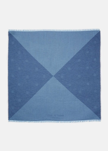 The Rag & Bone geo dagger scarf is square, features a geometric pattern with four blue triangular sections, faint repeating logos, and lightly fringed edges.