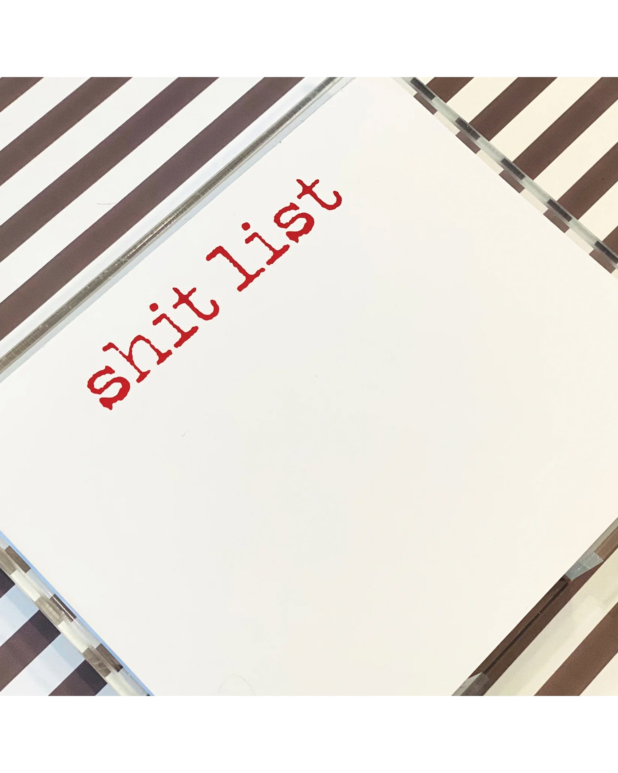 The Shit List NP by Black Ink is a luxe notepad with "shit list" in bold red lowercase on diagonal brown and white stripes—perfect as a cheeky gift or fun desk accessory.